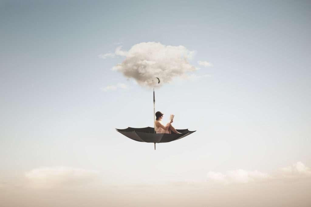 In a surreal, dream-like image, a woman sits reading a book in a large, upside-down umbrella that hangs in the sky by a cloud. 